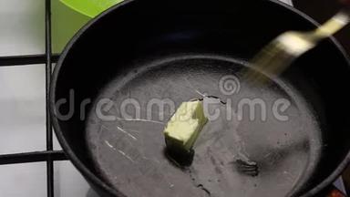 一块黄油在预热的锅里融化。 一个人用叉子抹它
